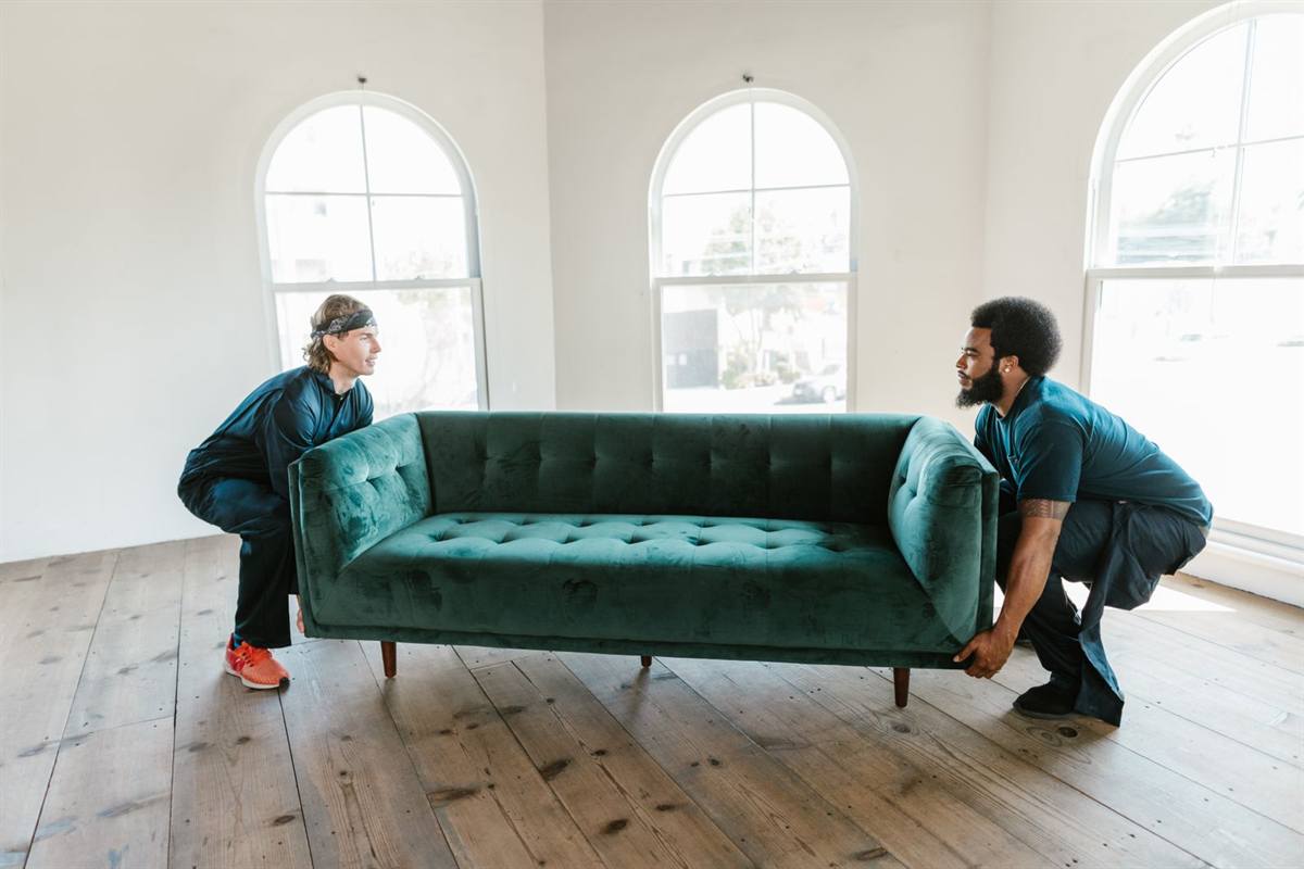 Two movers carrying a sofa through a room